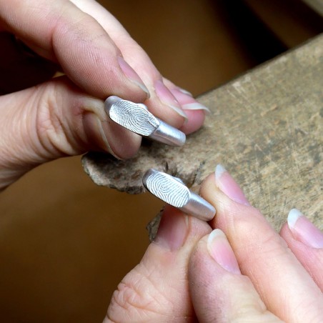 Photo dans les mains de deux chevalières en or gris fabriquées lors de l'atelier créer son alliance empreinte digitale.