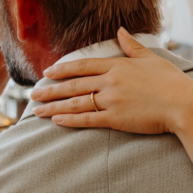 Photo d’une main de femme qui enlace un homme et qui porte à l’annulaire l’alliance originale or jaune modèle A 76.