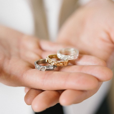 Photo des alliances homme modèle A76 dans différentes teintes de métal dans la main d’un homme. 